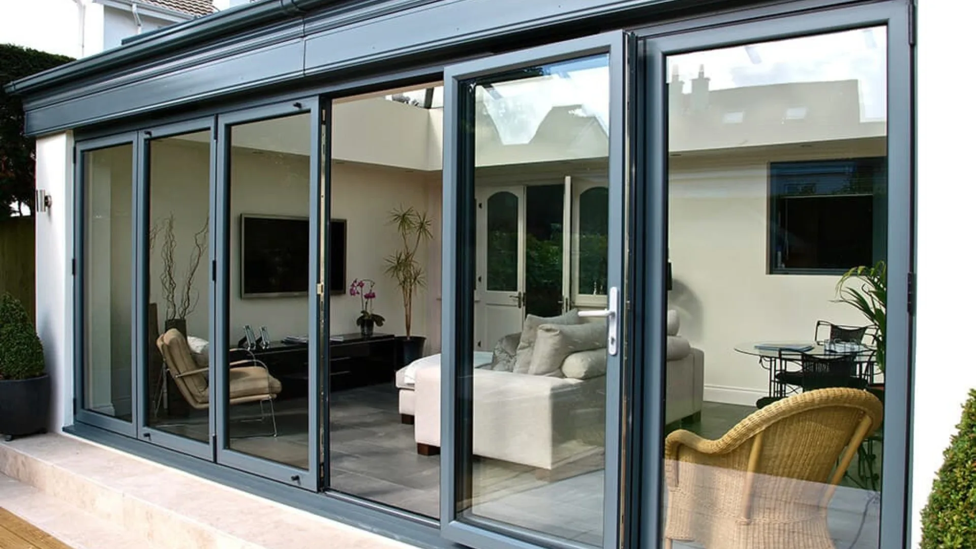 Aluminium folding doors opened to one side between a lounge and a garden, panels stacked flat