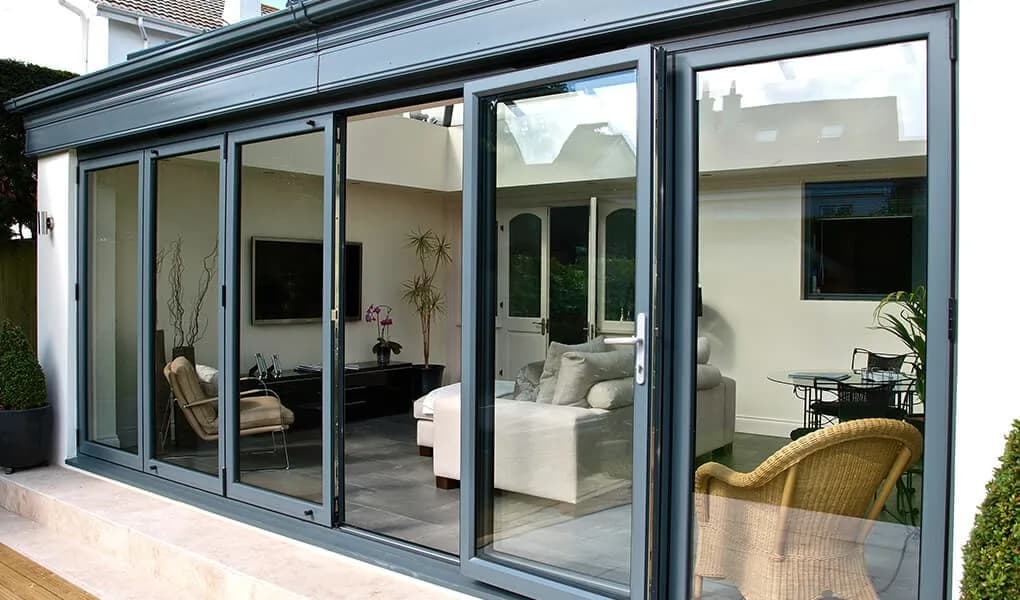 Grey aluminium bifold doors across the full width of a conservatory, half open