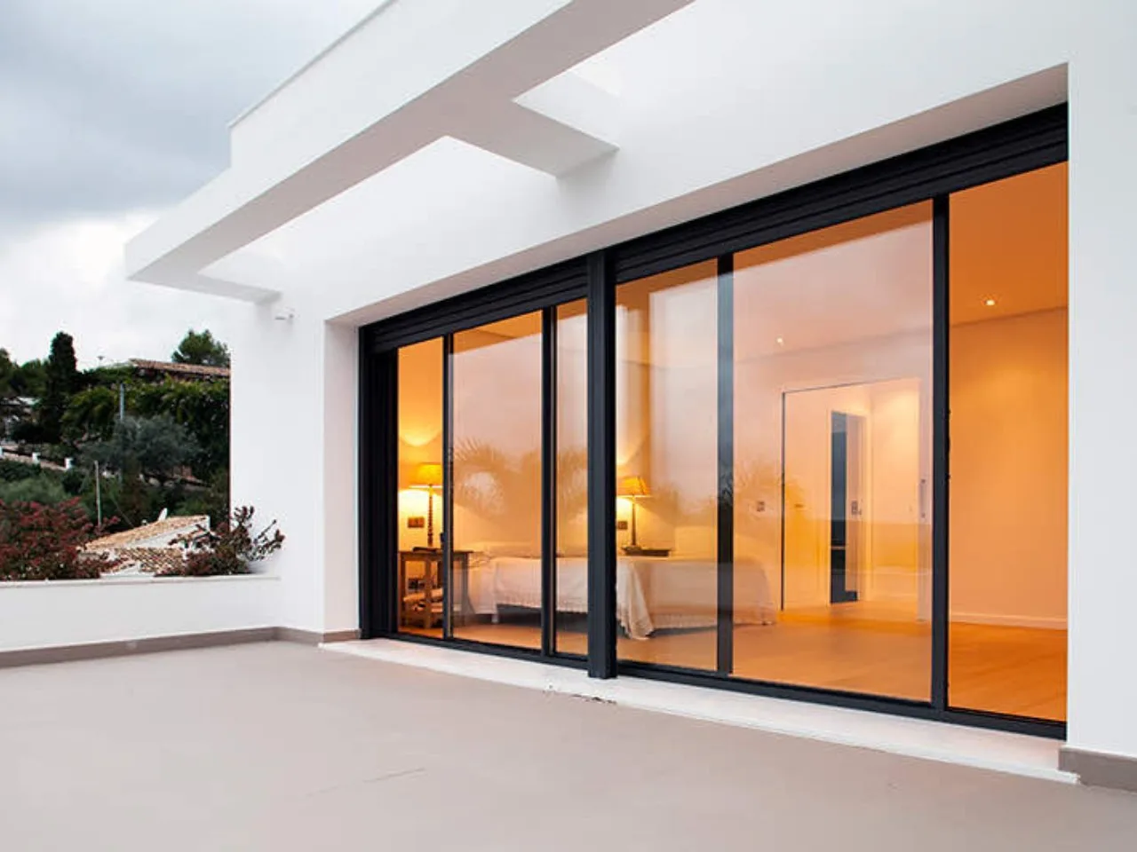 Minimal-frame sliding door on a white villa, warm interior light at dusk