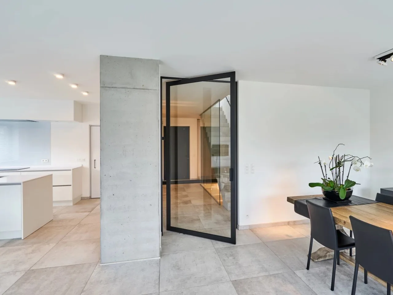 Glass pivot door between a kitchen and a dining room