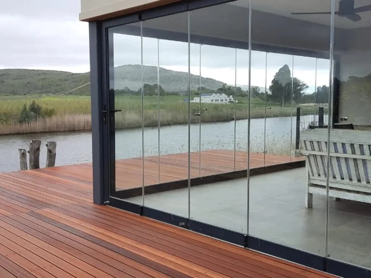 Frameless glass folding panels fully open on a lakeside deck