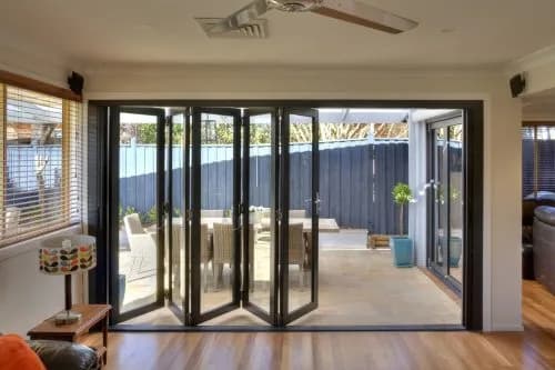 Black-framed bi-fold doors folded to the right, opening a dining area to a garden deck