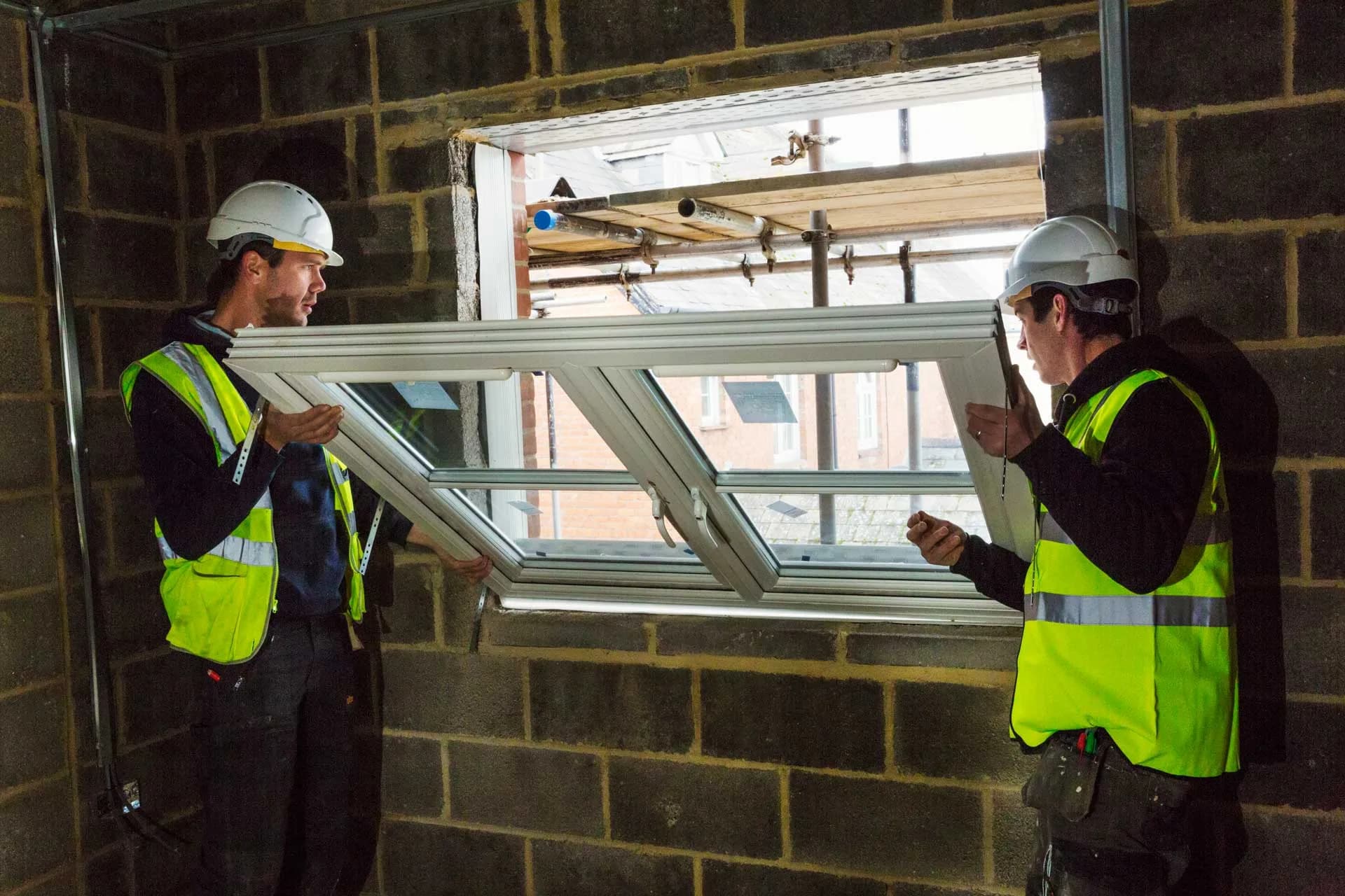 Two installers lifting a window frame into an opening